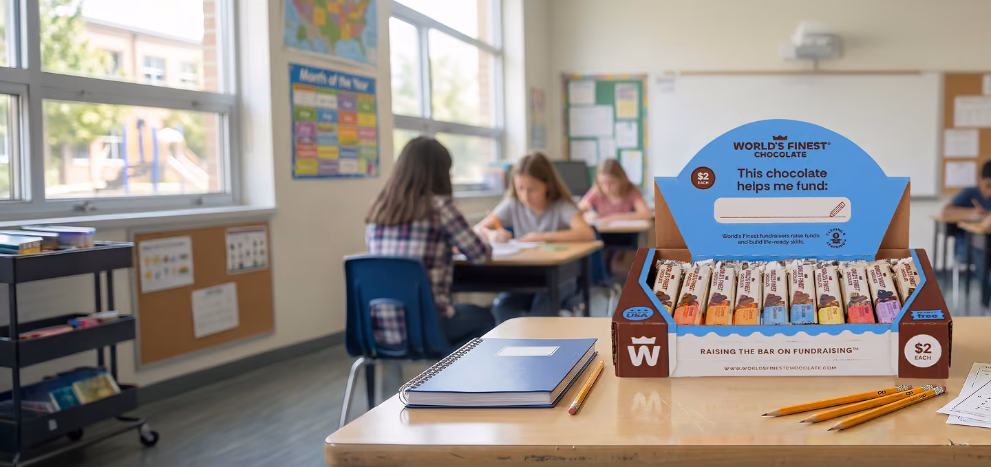 a box of WFC $2 dollar chocolate bars on a classroom desk with students in the background