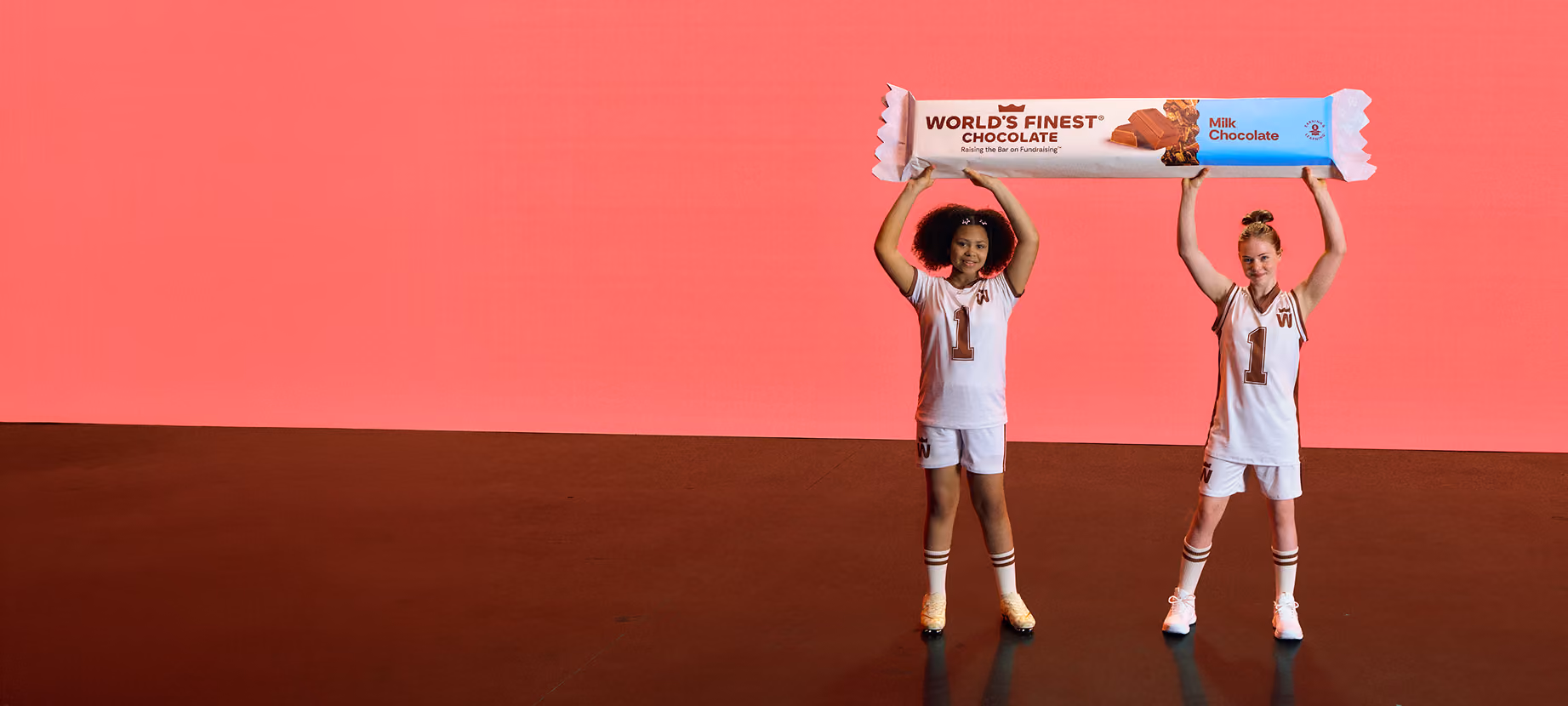 Two girls in basketball uniforms holding a oversized WFC chocolate bar over their head.