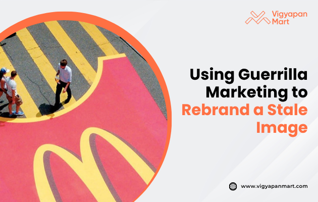 Aerial view of people walking on a street with a large, painted yellow "M" in a red area, resembling a well-known fast-food logo. Text on the right reads "Using Guerrilla Marketing to Rebrand a Stale Image." The tone is innovative and strategic.