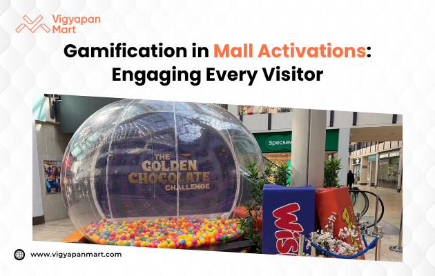 A large, transparent inflatable dome filled with colorful plastic balls in a mall setting. The dome displays 'The Golden Chocolate Challenge' text. The scene conveys an engaging and playful atmosphere, promoting gamification in mall activations. Vibrant brand signage and decorative plants are seen nearby.