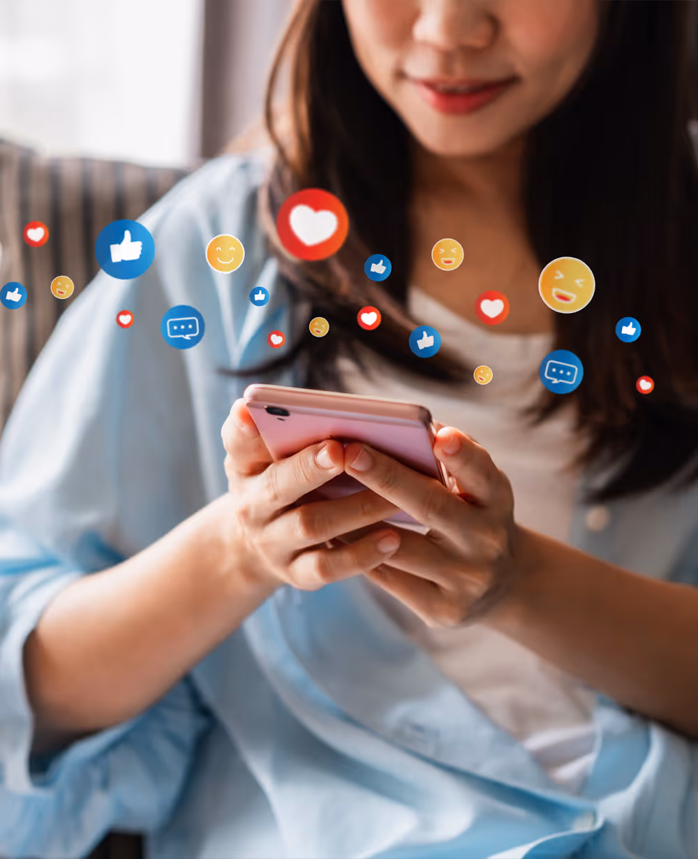Woman smiling while using a smartphone with floating social media reaction icons around her hands.