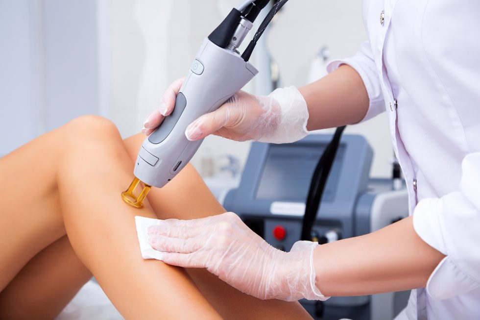Laser hair removal treatment on woman's legs at clinic, performed by professional wearing gloves
