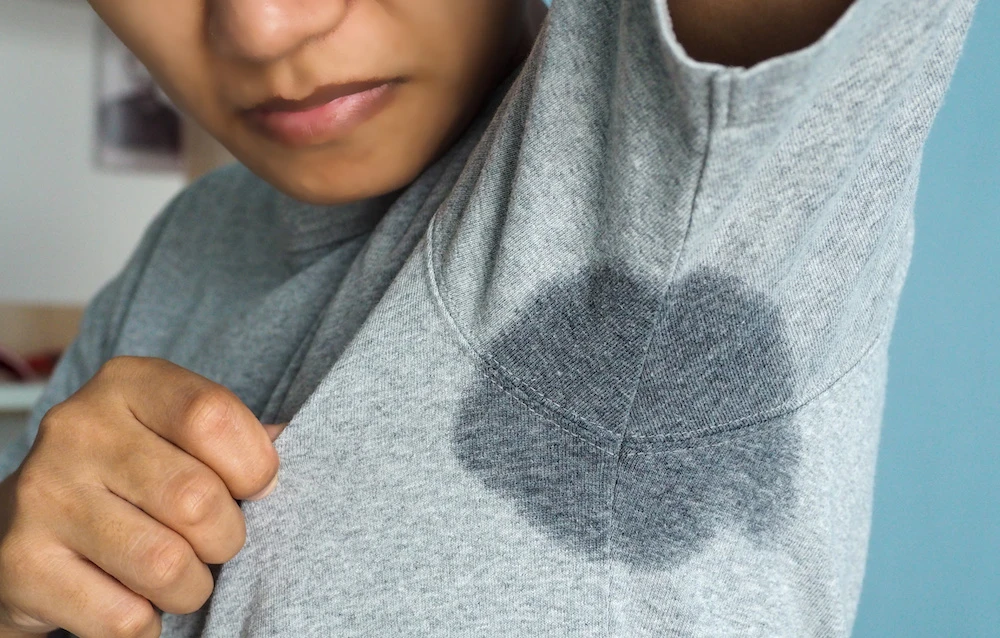 Person showing large underarm sweat stain on grey shirt, indicating excessive sweating or hyperhidrosis