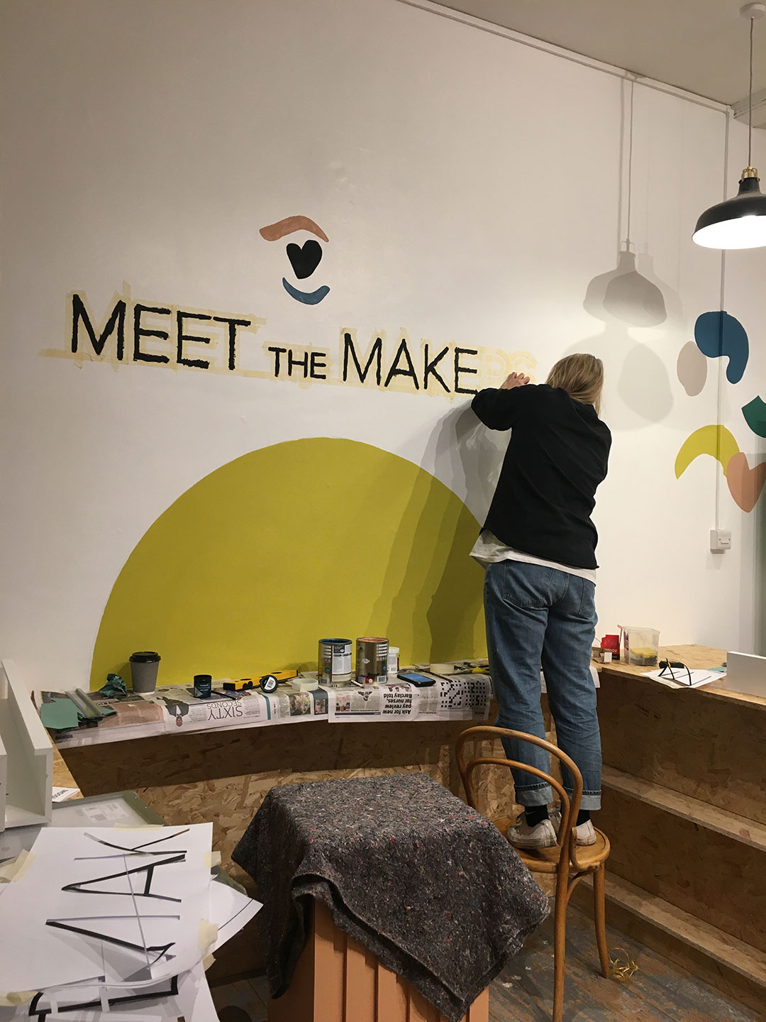 One person peeling off tape from a recently painted mural in a shop.
