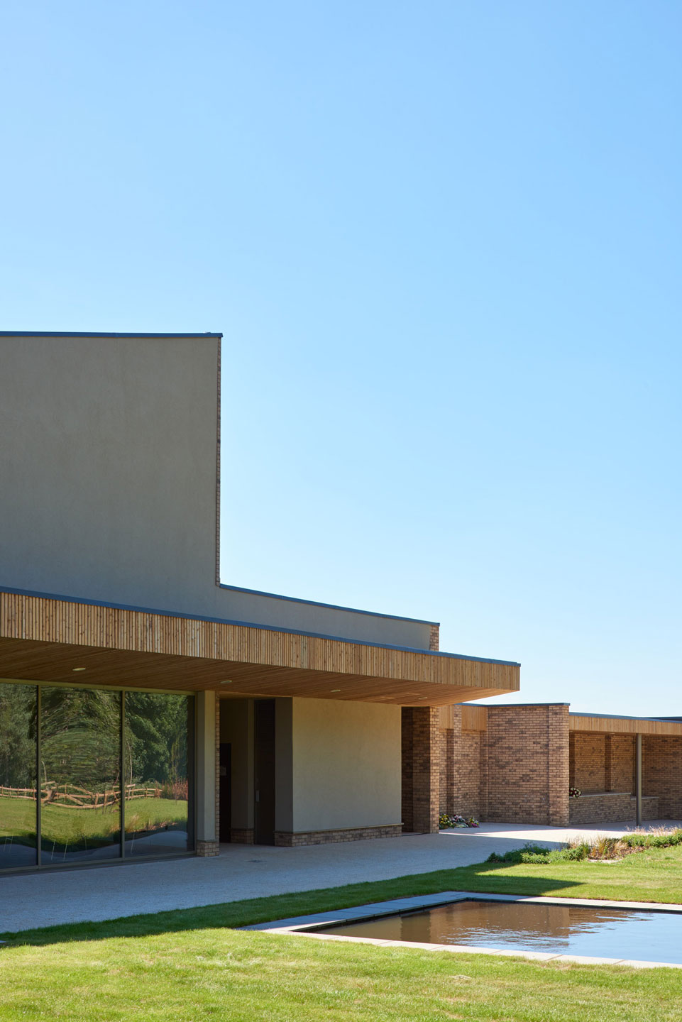 External view of modern brick clad building with large windows set within a landscaped garden with a water feature.