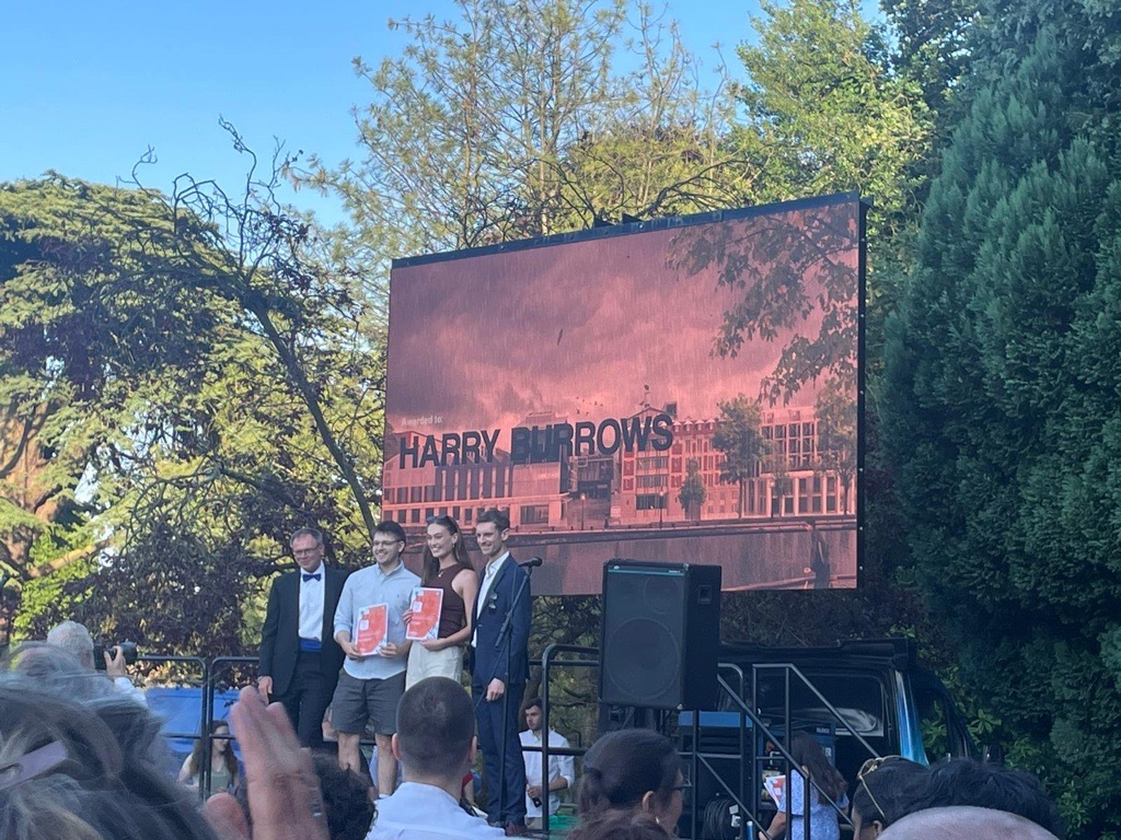 A photo of Ella on stage with her peers. A screen behind displays their work. 