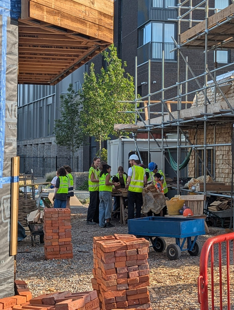 A photo of the Haverstock team brickmaking next to the community kitchen,
clad in sweet chestnut timber. To the right is the facade of the office.