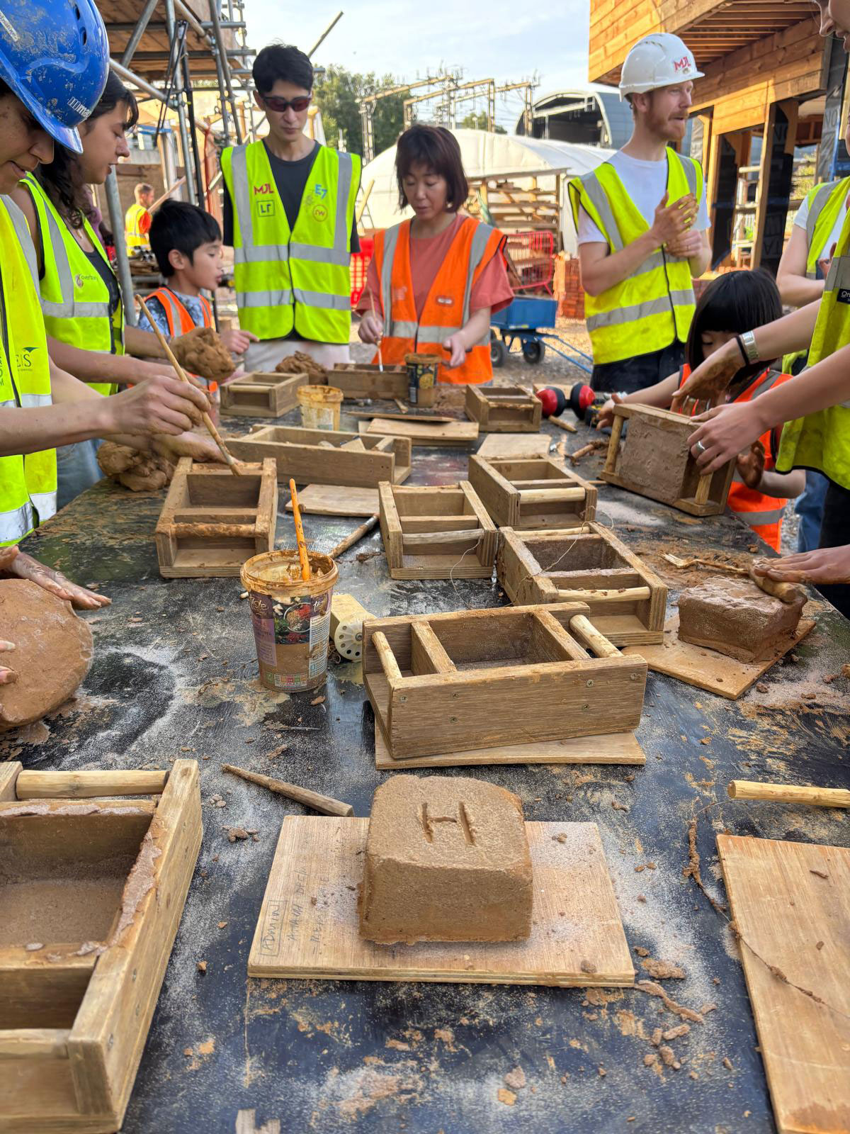 A completed handmade brick with an ‘H’ for Haverstock etched into the
surface. The table is covered in clay, slip and sand while the team works on their
handmade bricks.