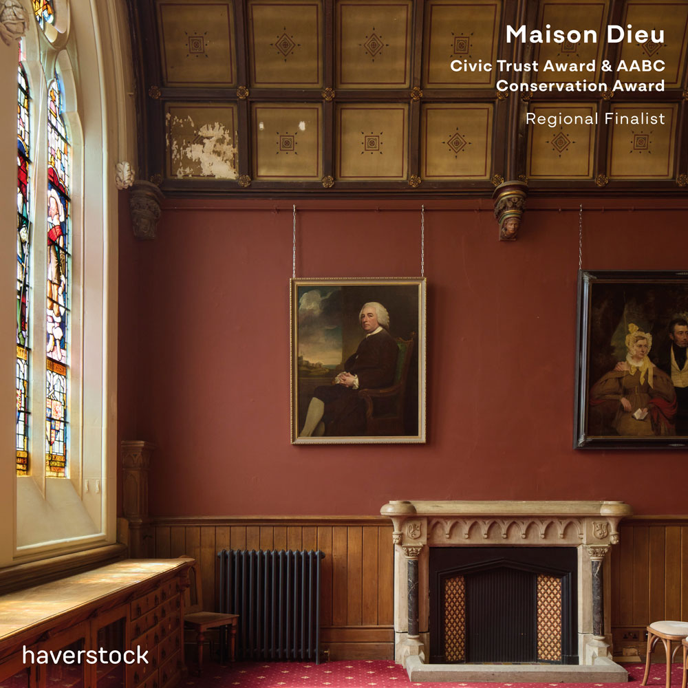 The council chamber. To the left is a large stained glass window. In the centre is a stone fireplace framed by
a burgundy wall. Paintings line the wall while the ceiling has decorative wooden panelling.