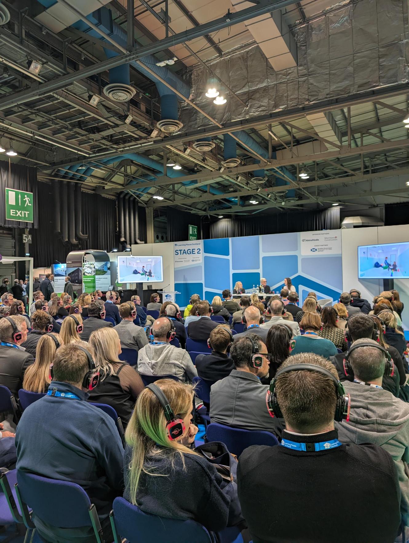 Another photo of the talk, from another angle. You can see guests watching,
the panellists present with screens either side. On the screen there is an internal photo
of an inclusive school.
