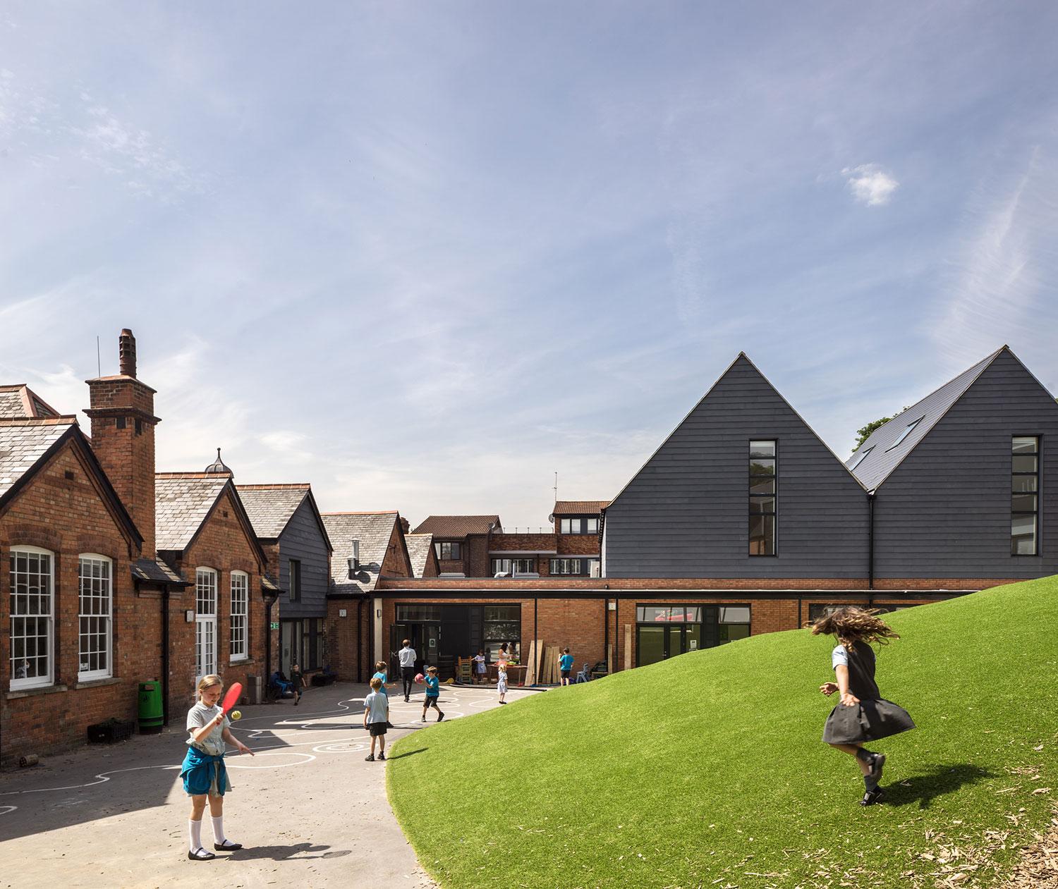 A photo illustrating where new additions meet the existing Victorian building. Black clad pitched roofs with double height windows mimic the historic form.