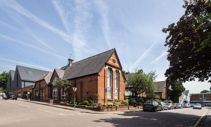 A photo of the existing red brick Victorian building, surrounded by mature trees.