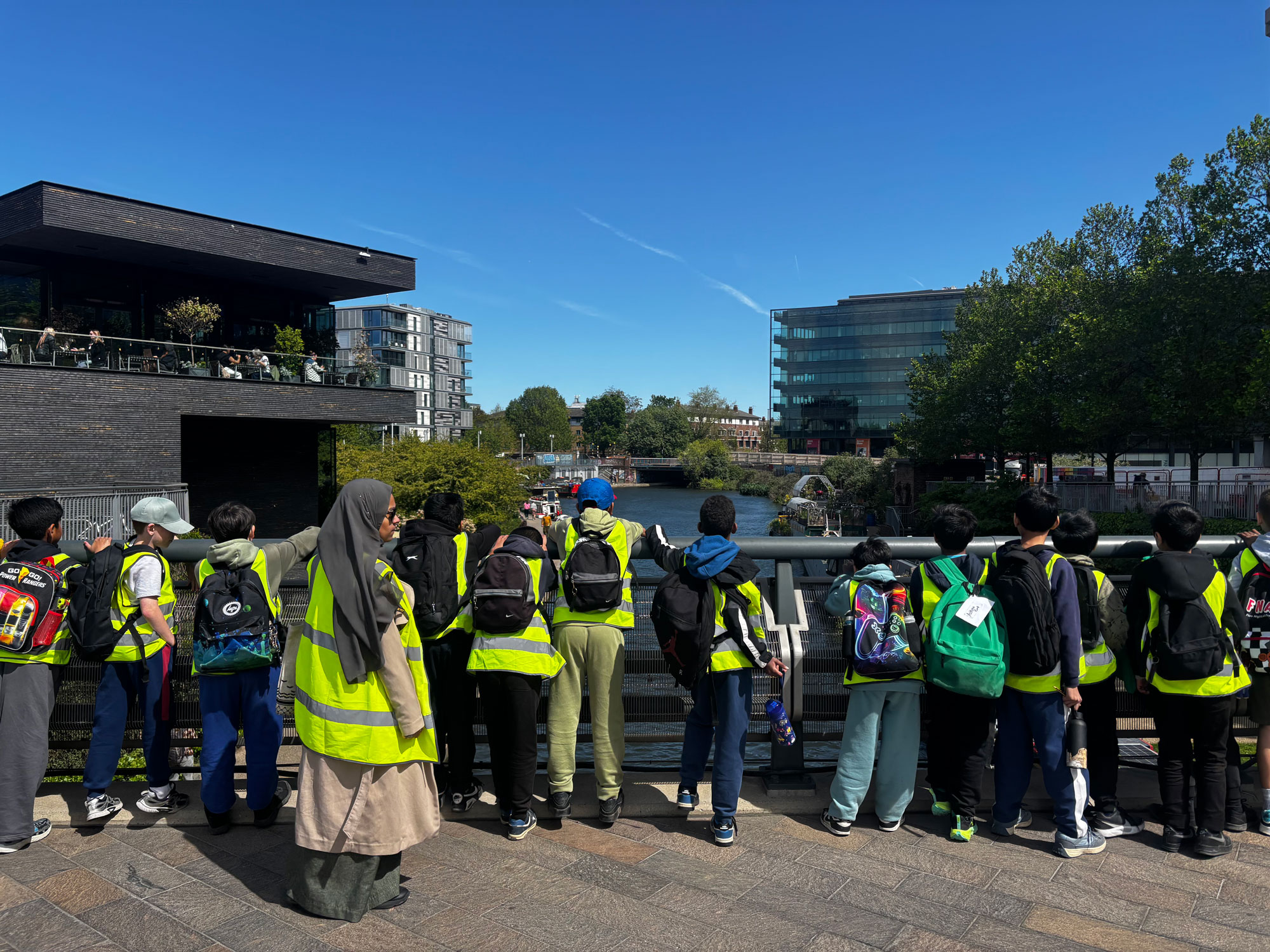 Students Observing the Floating Garden on the bridge at Coal Drops Yard. They wear hi-vis and face away from the camera, watching the water.