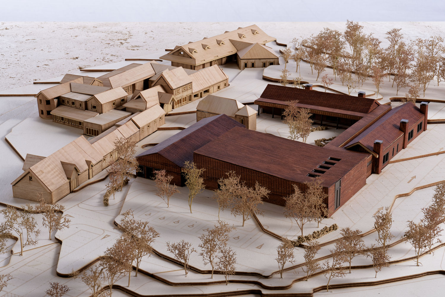  A view of the model depicting the proposed New Education Centre, the view is facing northwest. The existing thatched barn is to the left of the frame in a lighter wood, while the new centre is in a darker red-toned wood.