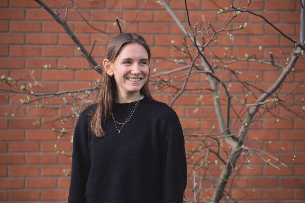 Photo of Nicole Johnson, Architectural Assistant at Haverstock, looking to the right of the camera and smiling, in front of a brick wall.
