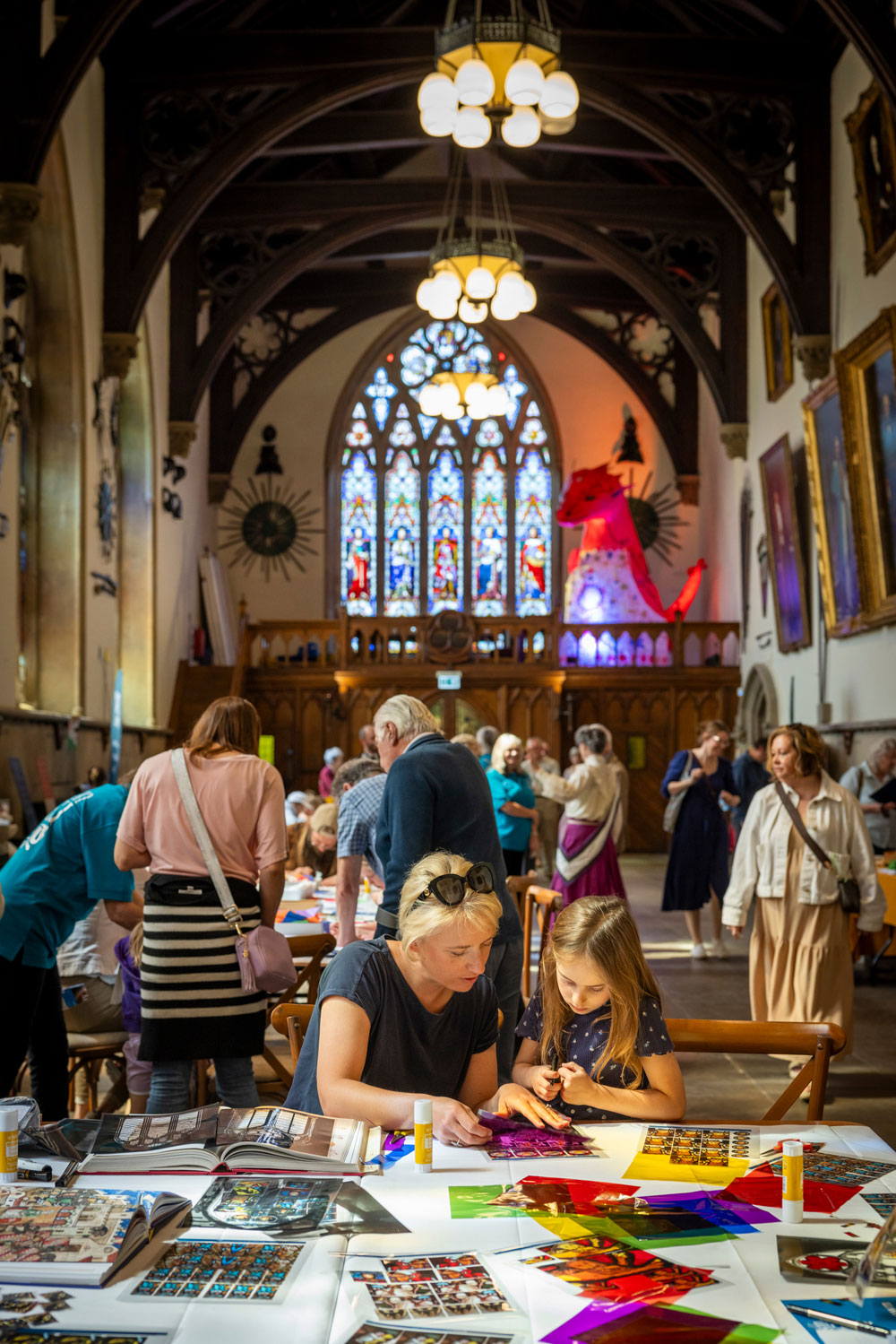 A woman and a child take part in the craft events, they are making a collage inspired by the large stained glass window behind them. 