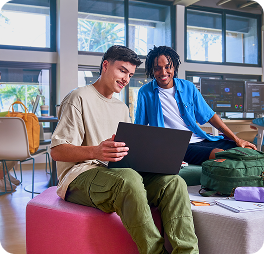 Dois estudantes em ambiente moderno de sala de estudo, sorrindo enquanto observam um notebook sobre o colo de um deles.