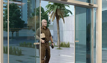 A man entering a modern building with glass sliding doors.