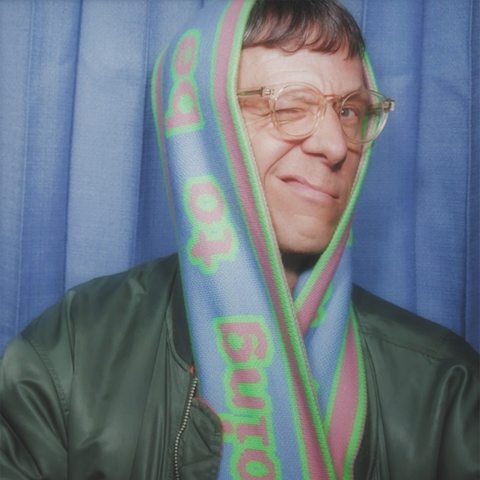 Beckmans Senior Lecturer Peter Ström with glasses wearing a colorful scarf wrapped around his head, winking, against a blue curtain background.