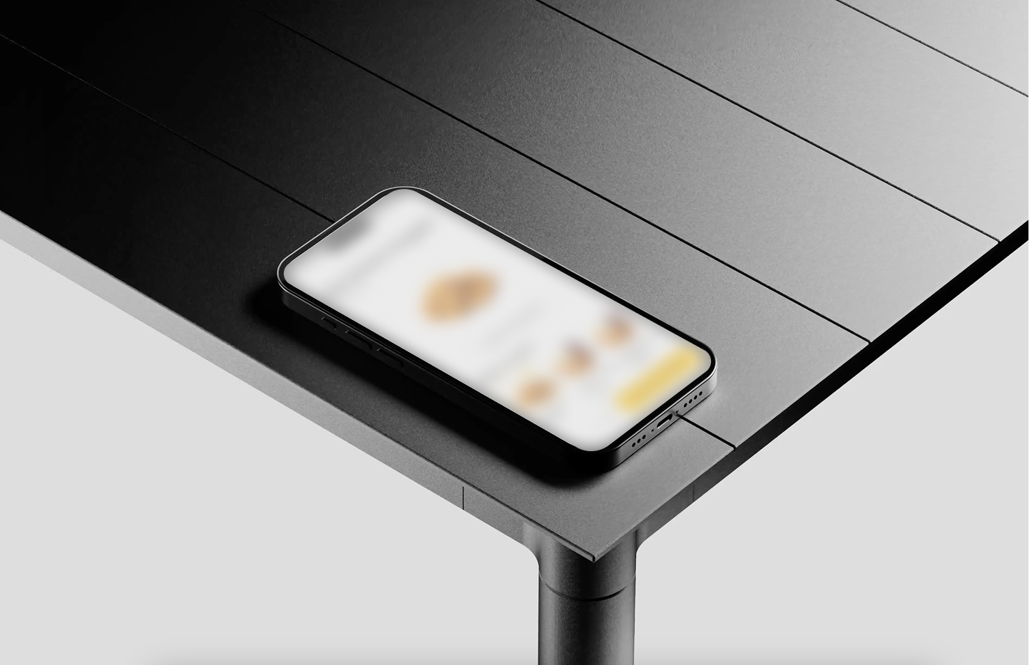 Black smartphone displaying a blurred app screen, resting on the corner of a dark gray modern table with a cylindrical metal leg.