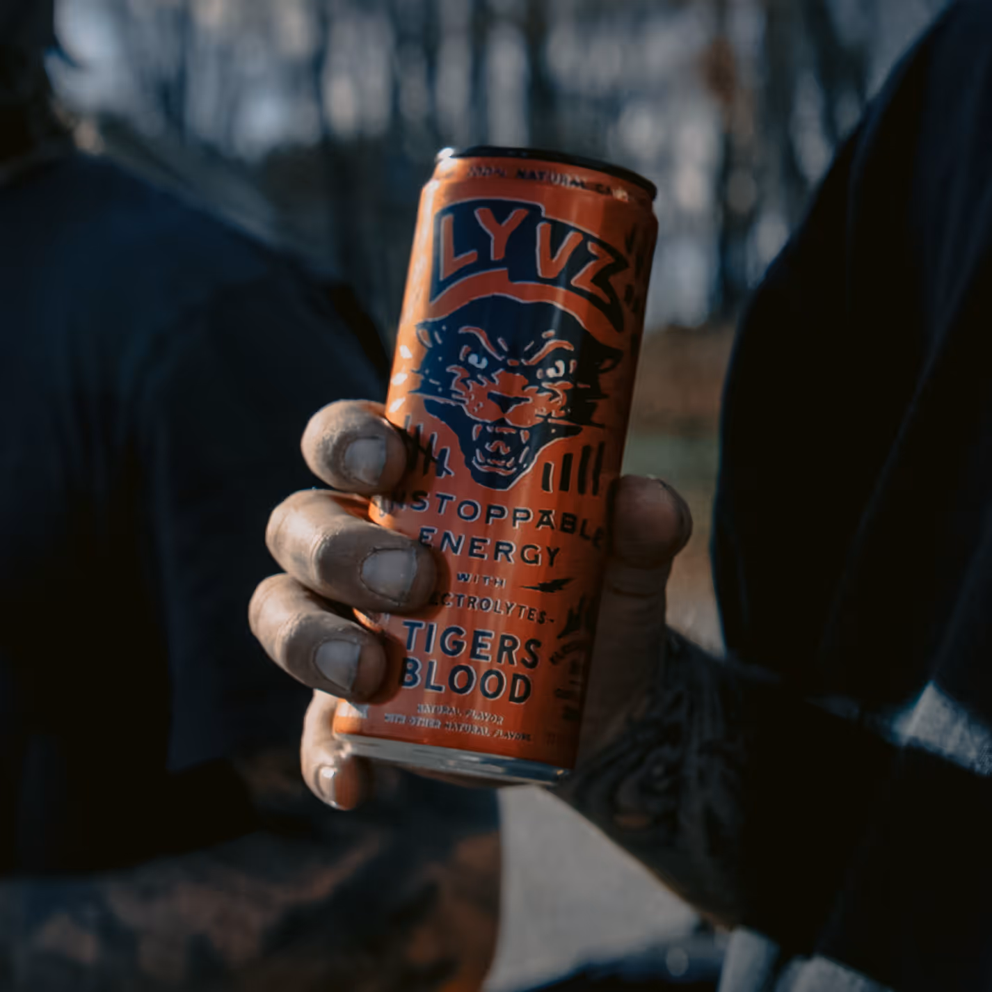 Hand holding an Tigers Blood energy drink can with tiger illustration and slogan that reads LYVZ Unstoppable Energy.