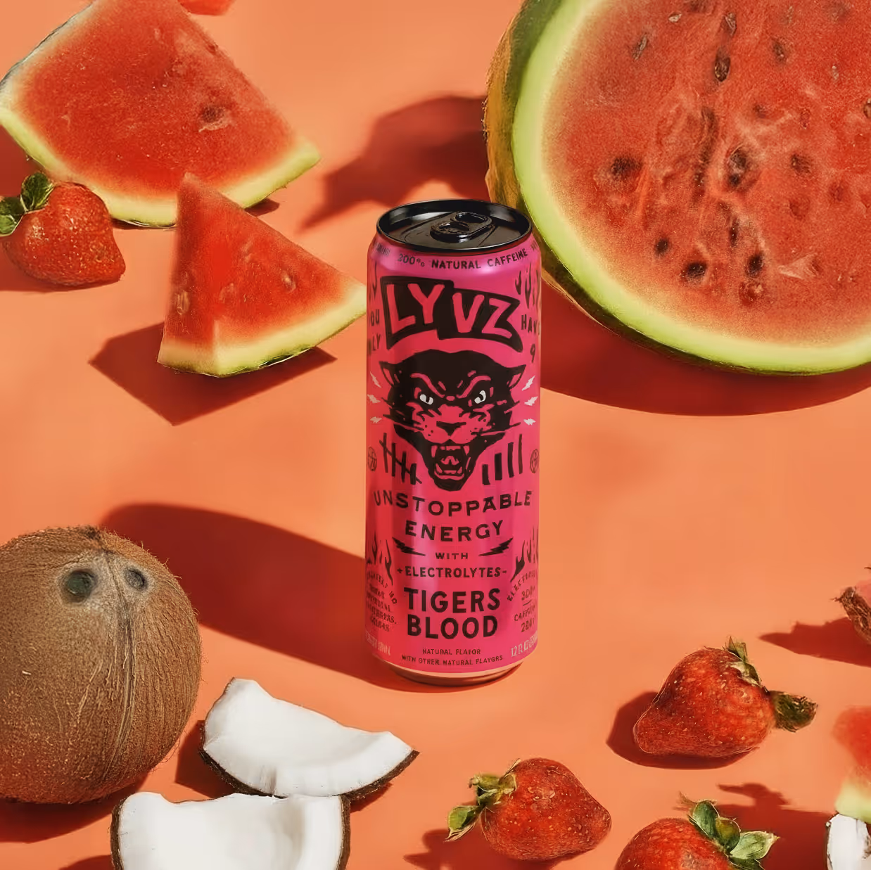 Red can of LYVZ Tigers Blood energy drink surrounded by watermelon slices, strawberries, coconut pieces, and a whole kiwi on an orange background.