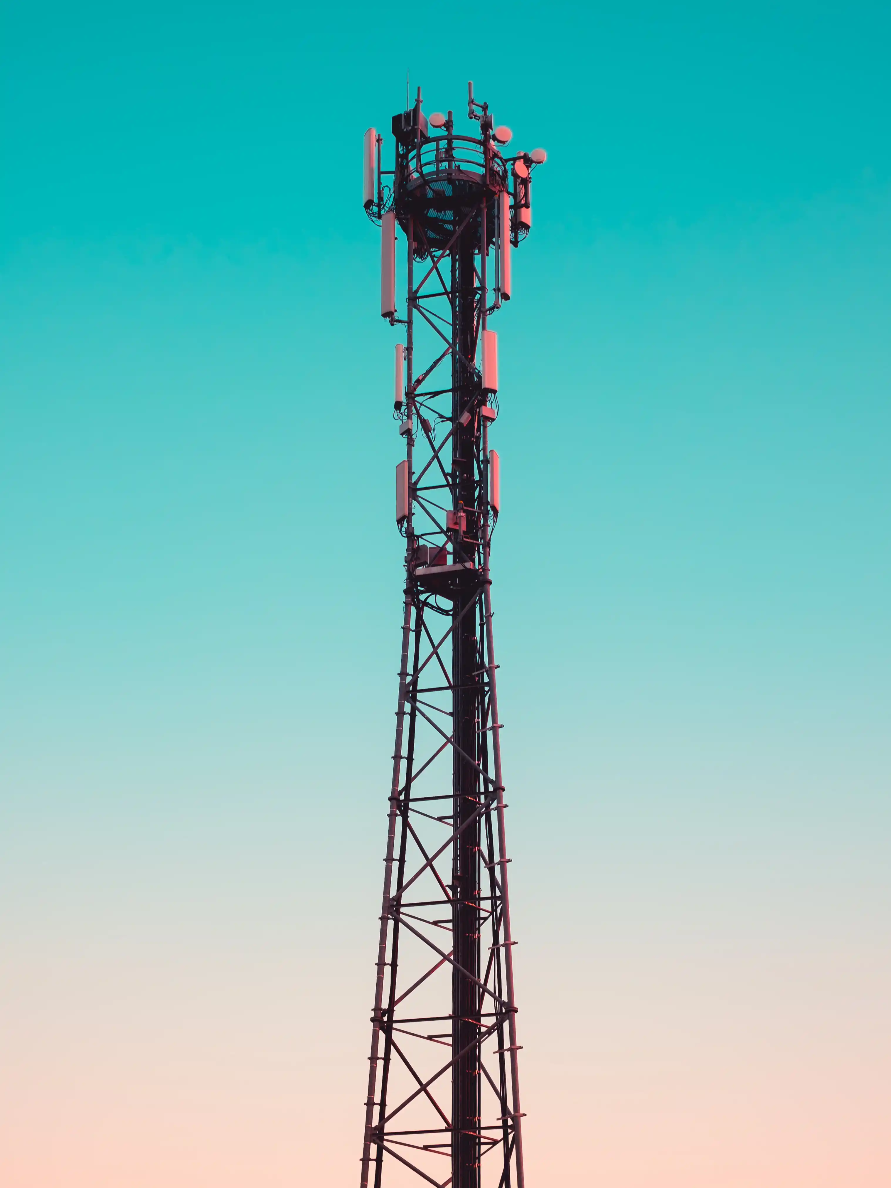 Tall telecommunications tower with antennas against a gradient sky transitioning from peach to turquoise.