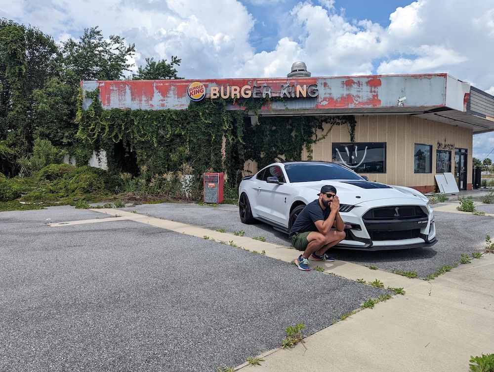 White sports car parked in front of abandoned Burger King restaurant with a man in front of the car