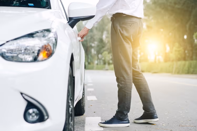 White car parked on street with person standing nearby in sunlight