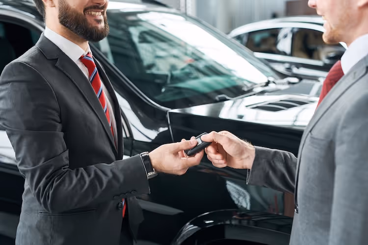 Car salesman handing over keys to customer in dealership showroom