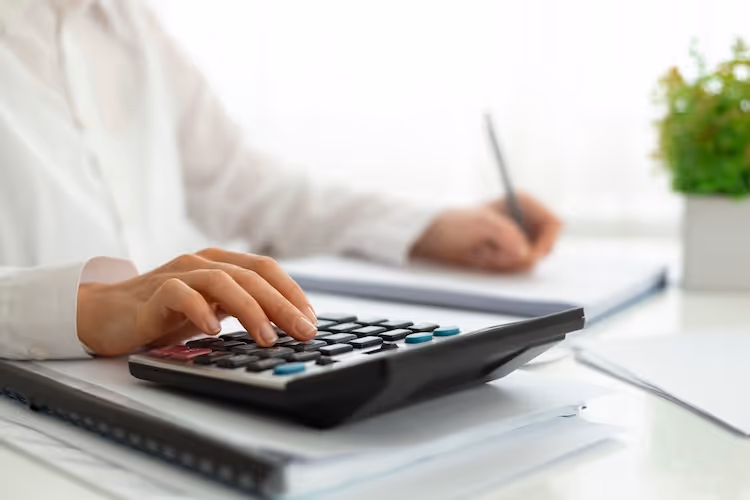 Person using calculator and taking notes at clean white desk