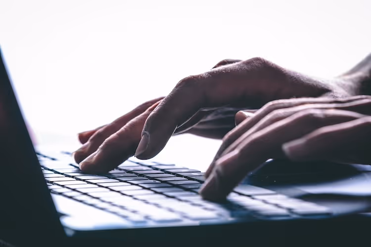 Hands typing on a laptop keyboard in low light