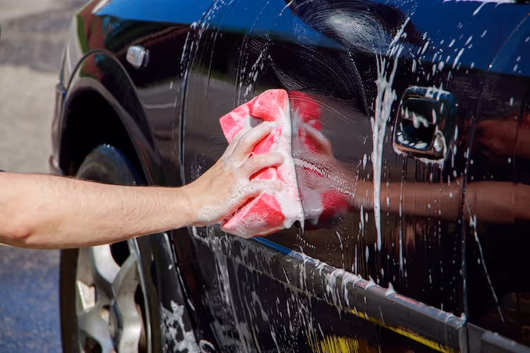 Hand washing car with pink soapy cloth, water splashing
