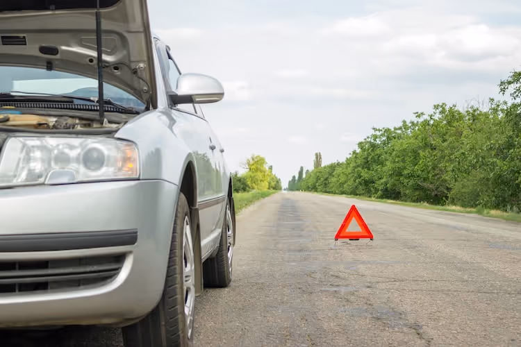 Broken down car with open hood and warning triangle on rural road