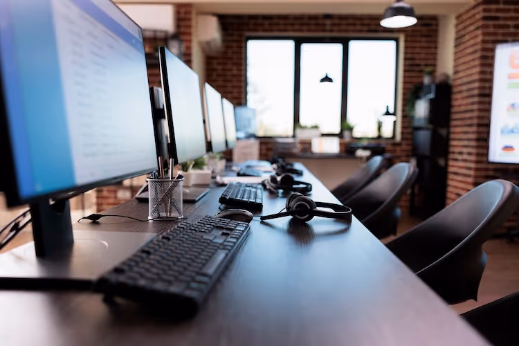 Modern office workspace with computers, headphones, and brick wall background