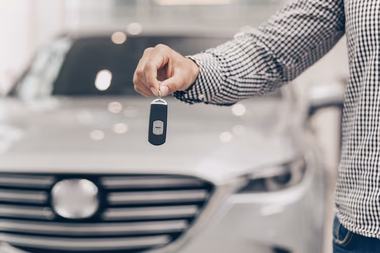 Hand holding car key fob in front of new vehicle at dealership
