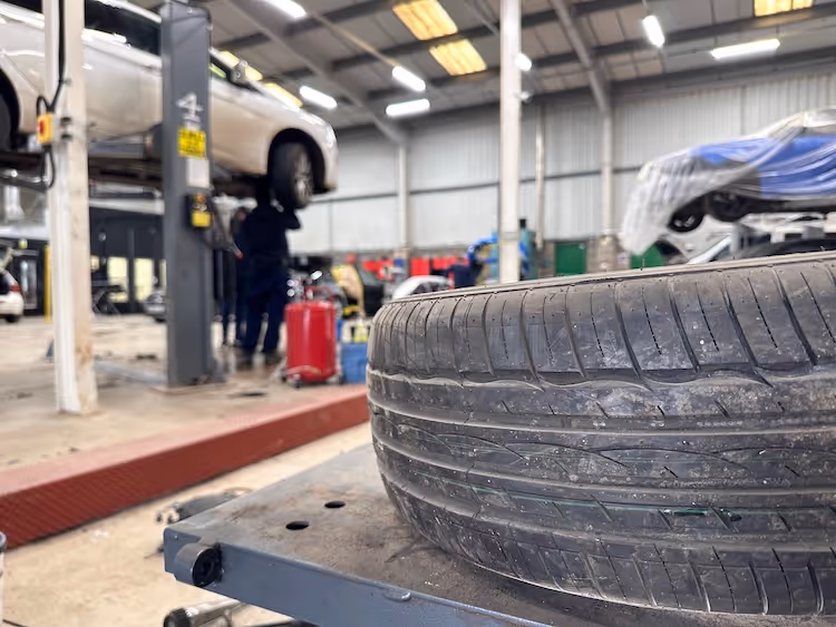 Used tire in foreground with car lifted on hydraulic lift in auto repair shop
