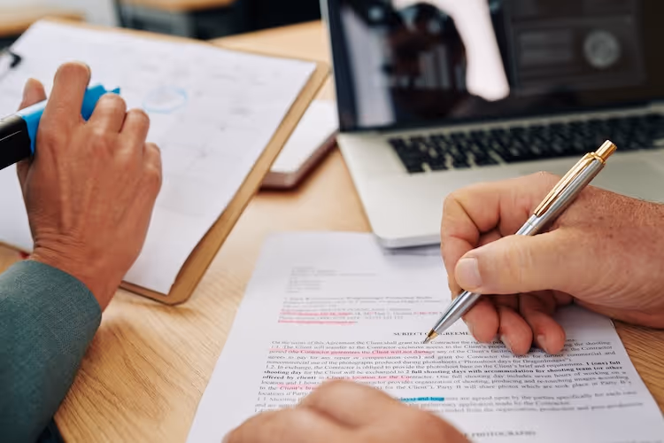 Hands working on document with laptop, pen, and highlighted text