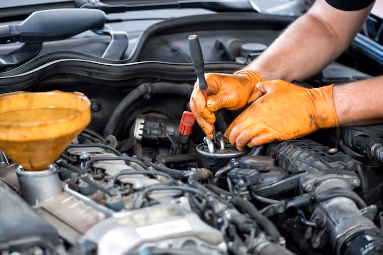 Mechanic in orange gloves repairing car engine under the hood