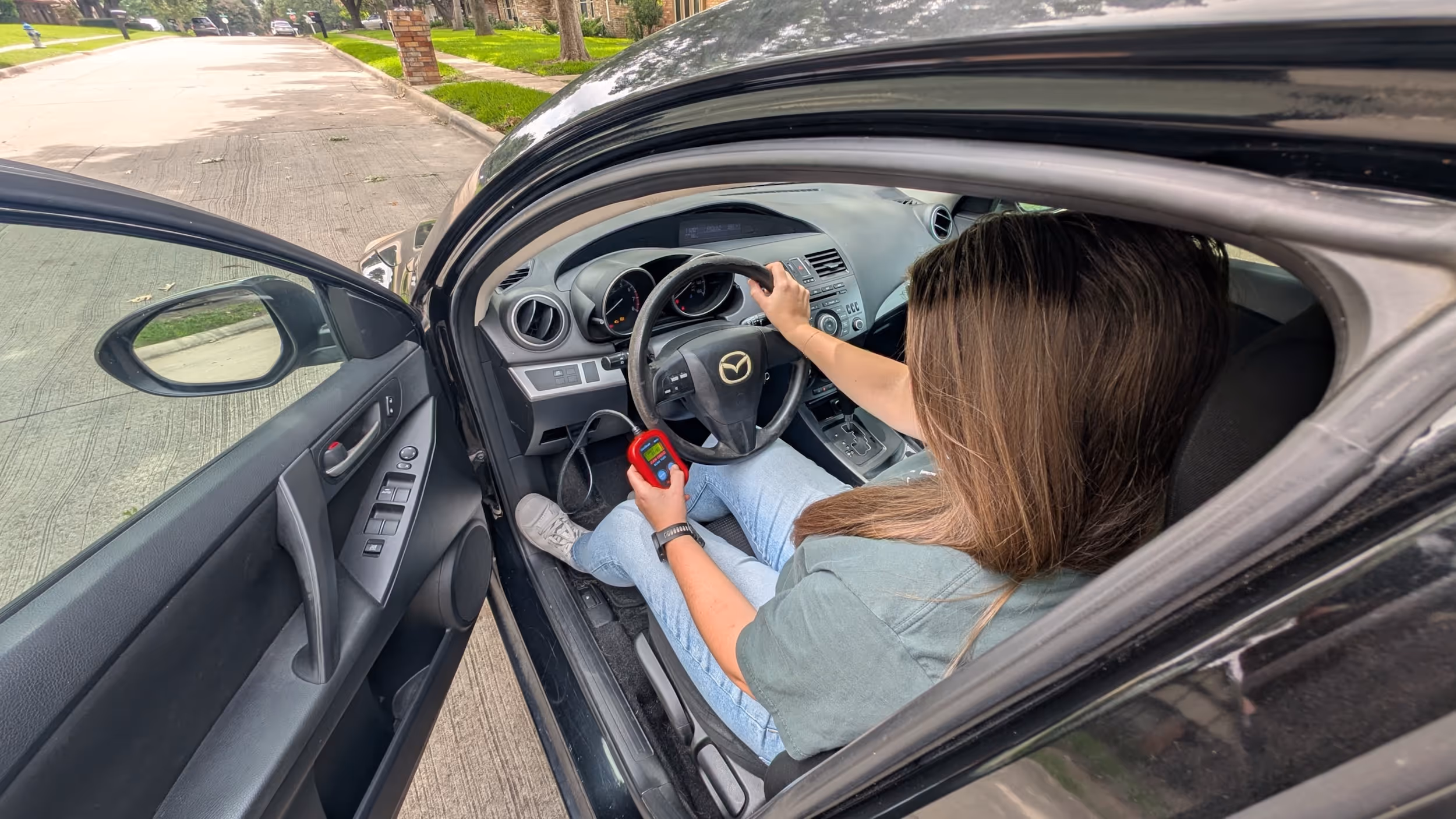 Person sitting in Mazda car, holding a red device while parked