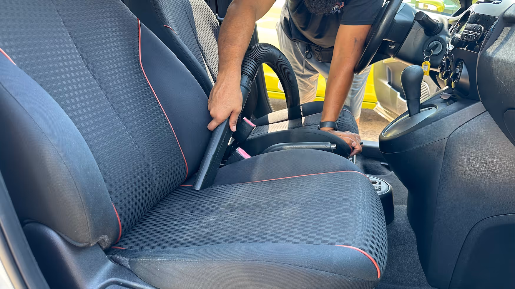 Vacuuming car seats with a black handheld vacuum cleaner