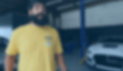 Person in yellow shirt standing in blurry automotive workshop background