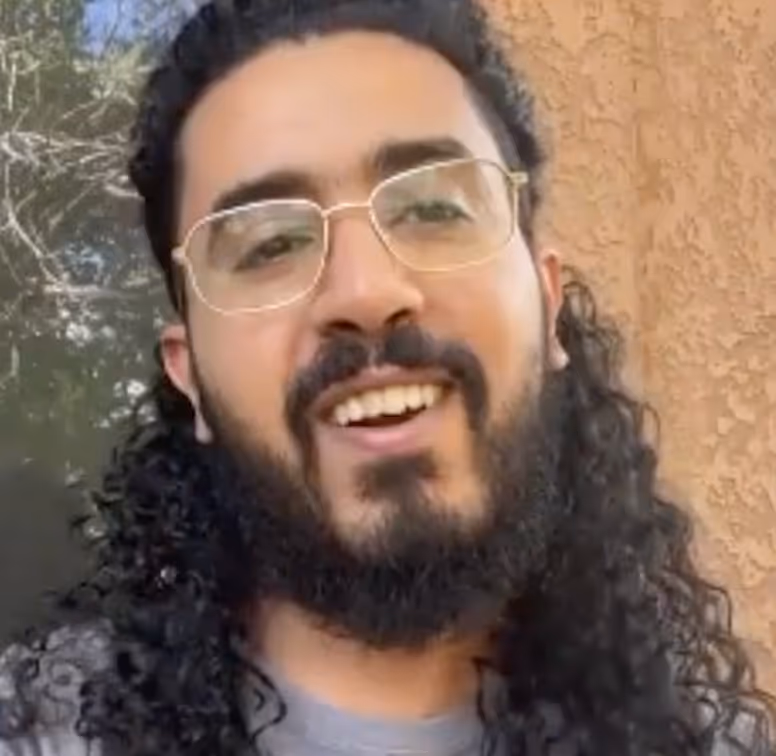 Person with glasses and long curly hair smiling outdoors