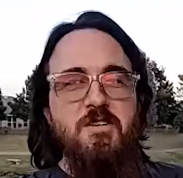 Person with glasses and long hair outdoors, looking at camera