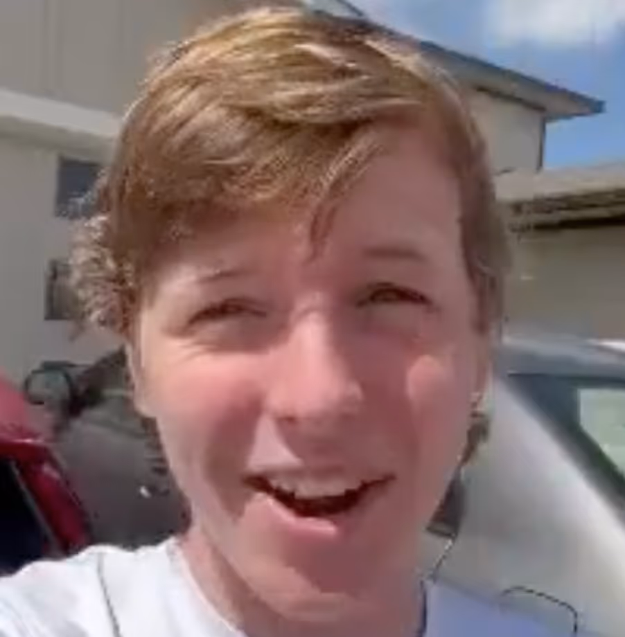 Person with short hair laughing outdoors on a sunny day