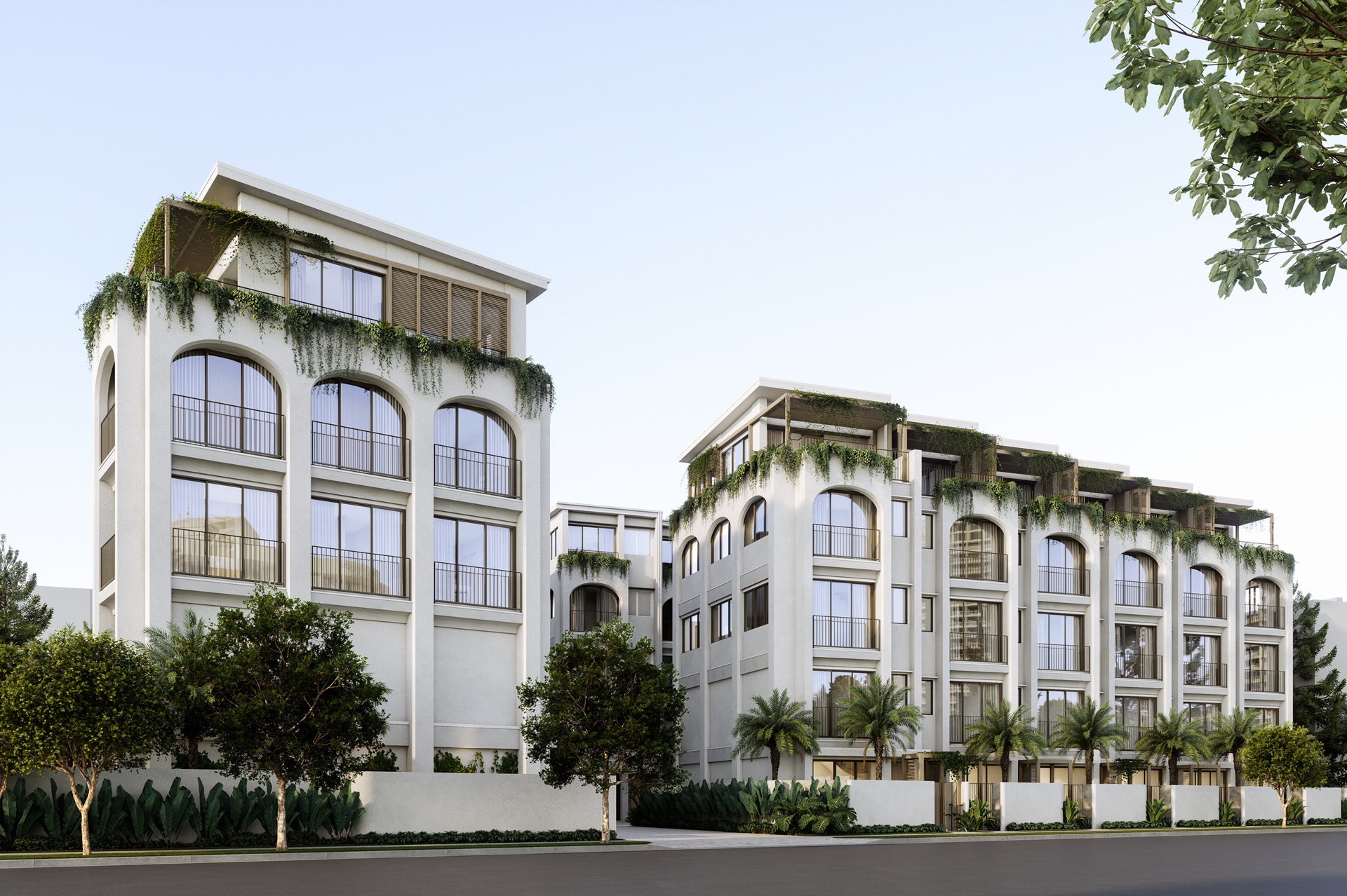 Modern white residential buildings with large arched windows and green plants cascading from planters, surrounded by palm trees and other greenery under a clear sky.