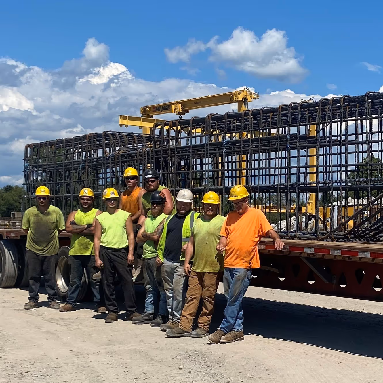 Workers posing in front of large prefabricated reinforcing bar on a truck bed