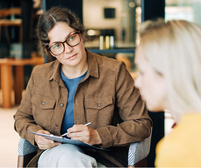 Therapist attentively listening and taking notes while a patient speaks during a counseling session.