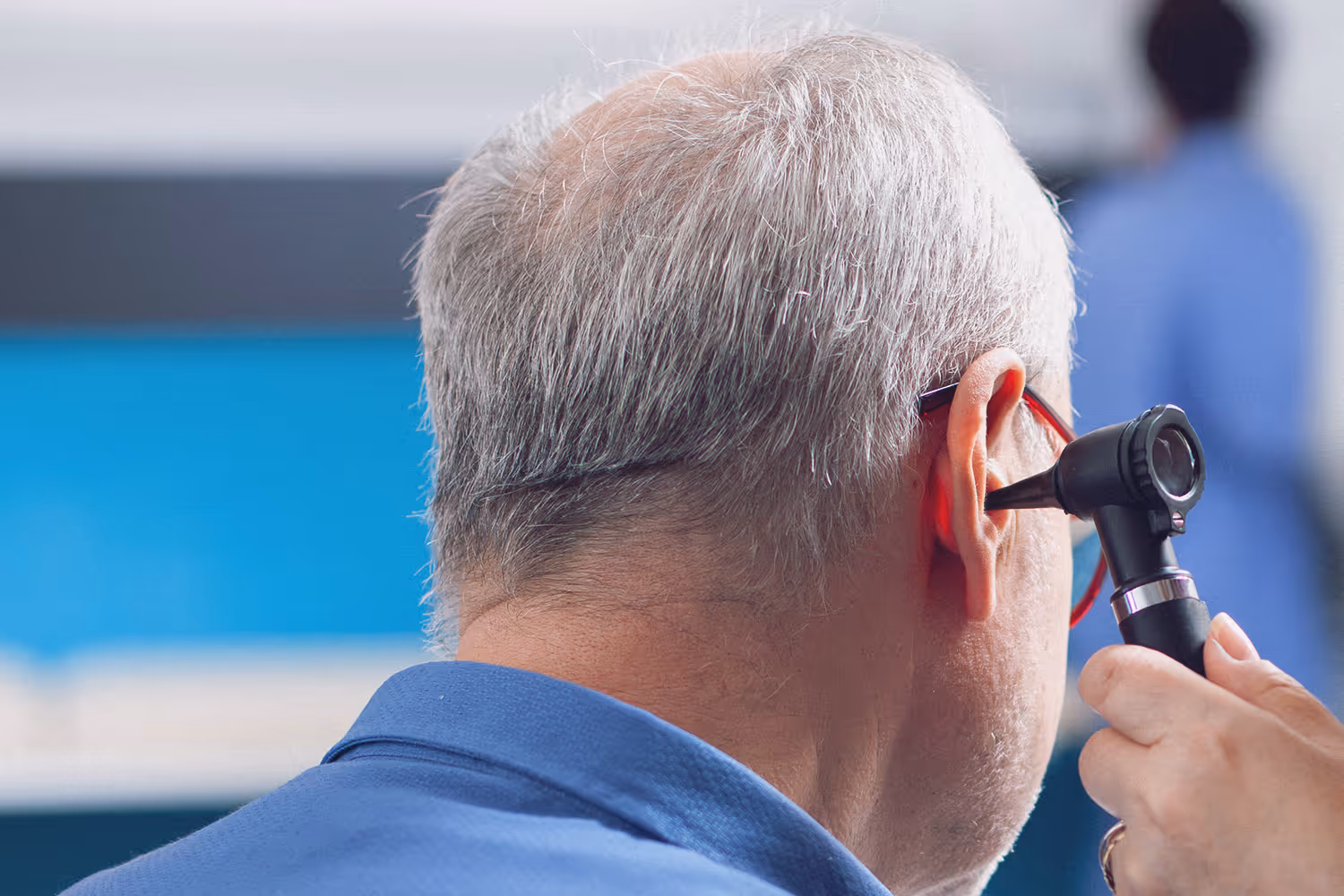 Ear examination of a man with gray hair using an otoscope by a medical professional.