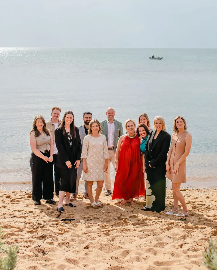 PIER team standing on a sandy beach with calm water and a small boat in the background.
